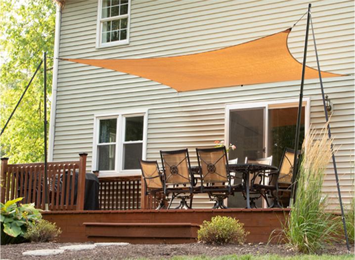 An orange shade sail held up by black Carbiepoles is mounted over a outdoor dining area of a home.